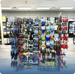 Pet store display with assorted toys, including balls, chew toys, and ropes, on a wire rack. The scene is colorful and neatly organized, evoking a sense of fun.