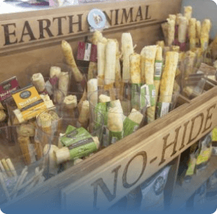 Wooden display. holding assorted Earth Animal No-Hide dog chews in varying sizes and packaging, conveying a natural and pet-friendly vibe.