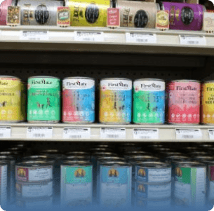 Cans of pet food displayed on supermarket shelves, arranged in vibrant colors like green, blue, yellow, and pink. Labels are visible, creating a lively scene.